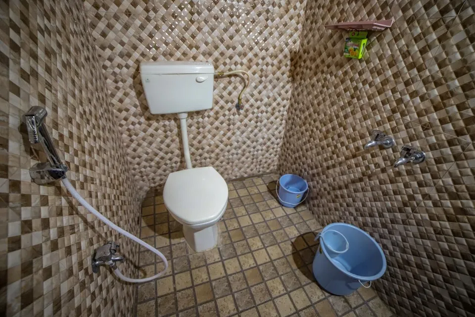 A bathroom with diamond-patterned wall tiles, a hand shower and buckets