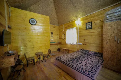 The Wooden Cottage bedroom: a double bed under a high pitched ceiling, with timber-panelled walls